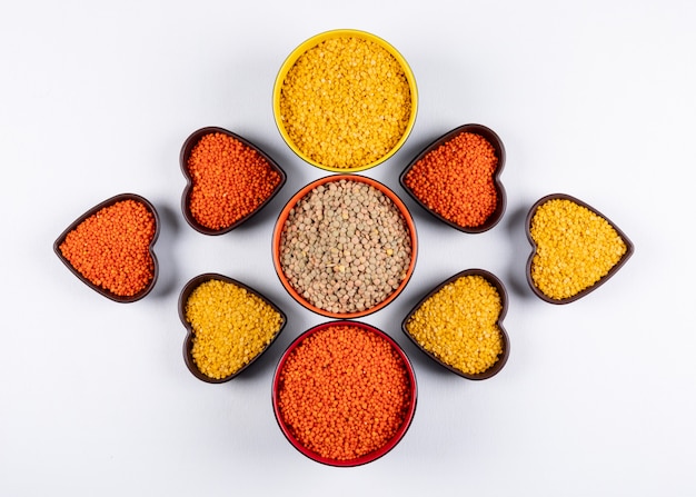 Free photo top view red, yellow and green lentils in different colored and heart shaped blows