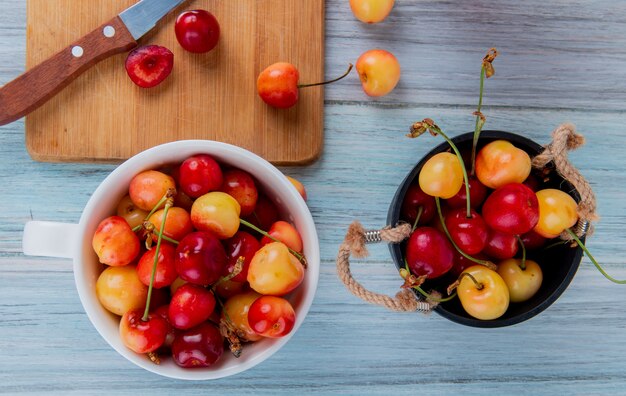 Top view of red and yellow ripe cherries in a bucket and rainier cherries in a bowl on rustic wood