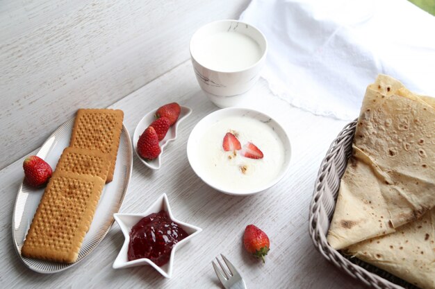 Top view of rice porridge with milk and strawbwrries served with jam and cookies on white