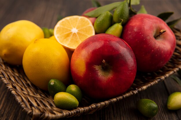 Top view of rich in vitamin fruits such as apples lemons and kinkans on a wicker tray on a wooden surface