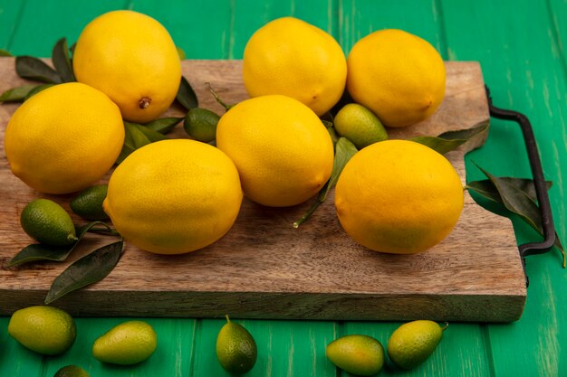 Вид сверху богатых витаминами фруктовых лимонов с листьями, изолированными на деревянной кухонной доске на зеленой деревянной стене