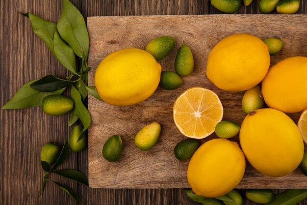 Вид сверху на богатые витаминами фрукты, такие как кинканы и лимоны, изолированные на деревянной кухонной доске на деревянной стене