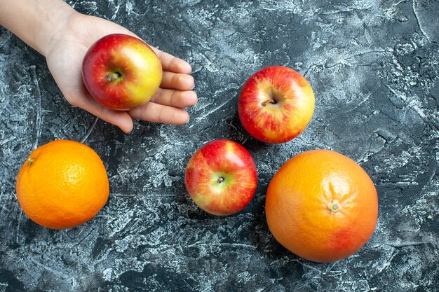 Top view ripe apple in female hand oranges and apples on grey background