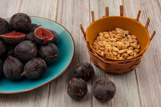 Free photo top view of ripe black mission figs on a blue bowl with peanuts on a bucket on a grey wooden wall