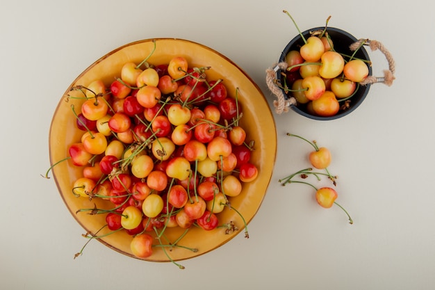 Top view of ripe rainier cherries in a bowl and bucket on white