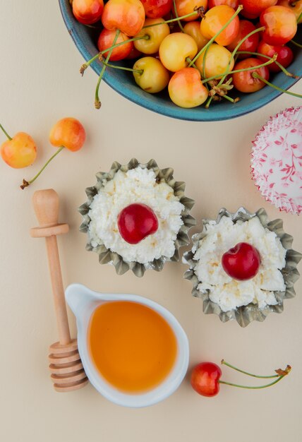 Top view of ripe rainier cherries in a bowl with cottage cheese in mini tart tins and honey on white