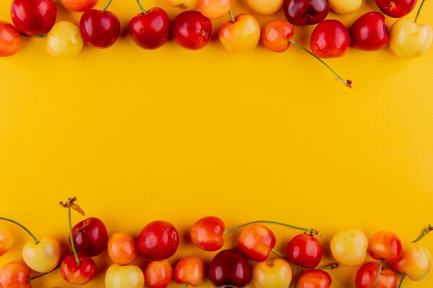 Top view of ripe red and yellow cherries isolated on yellow with copy space