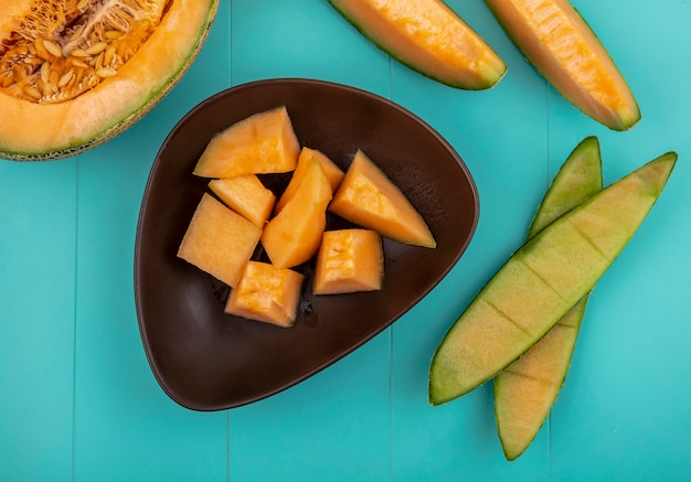 Top view of ripe sweet cantaloupe melon slices on a brown bowl on blue surface