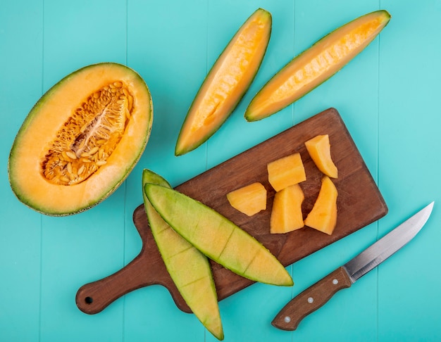 Top view of ripe sweet cantaloupe melon slices on a wooden kitchen board on blue surface