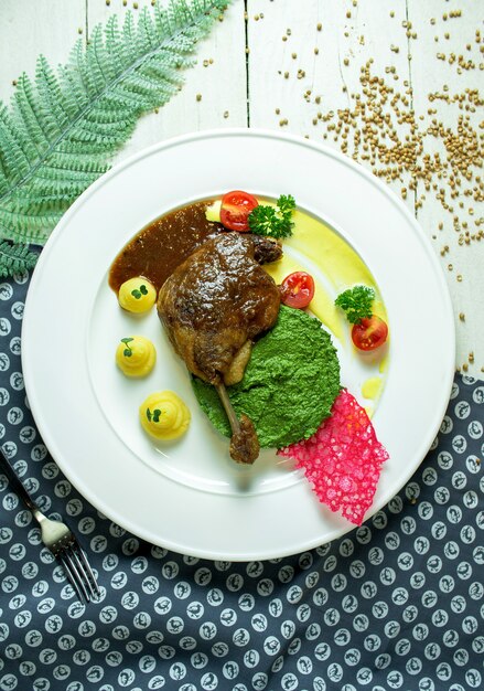 Top view of roast duck leg with avocado sauce and mashed potatoes with cherry tomatoes on a white plate