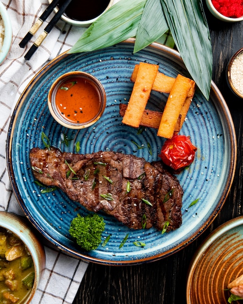 Free photo top view of roasted beef with spicy sauce and grilled tomato with fried bread sticks on a plate