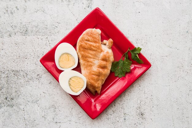 Top view of roasted chicken wings with boiled egg in red plate over concrete floor