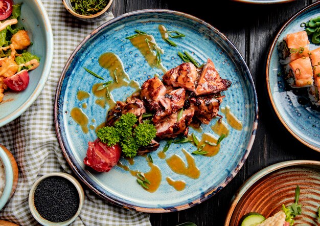 Top view of roasted chicken with grilled tomato fresh herbs and sauce on a plate on wood