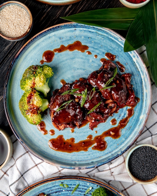 Free photo top view of roasted chicken with sweet and sour sauce and broccoli on a plate on wooden surface