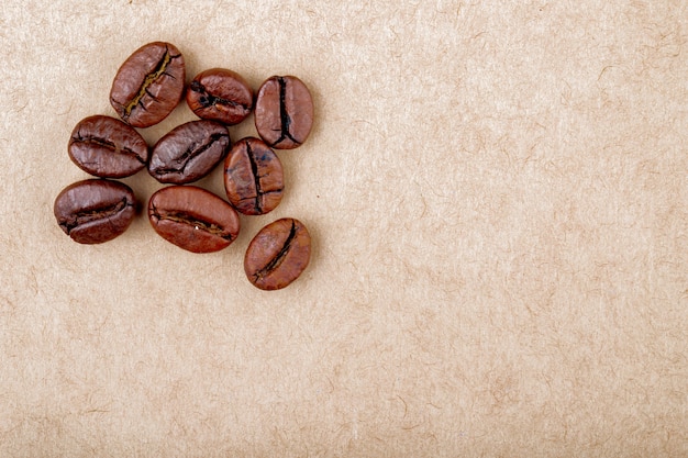 La vista superiore dei chicchi di caffè arrostiti ha isolato il fondo di struttura della carta marrone con lo spazio della copia