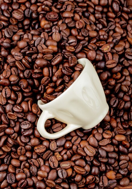 Top view of roasted coffee beans scattered from a ceramic cup on coffee beans