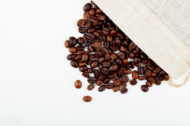 Top view of roasted coffee beans scattered from a sack on white background with copy space