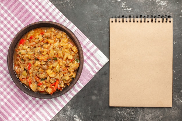 Free photo top view of roasted eggplant salad in bowl a notebook on dark surface