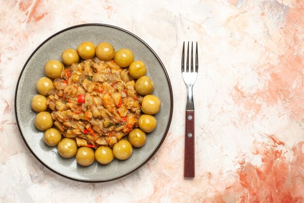 Top view of roasted eggplant salad and pickled plums on plate fork on nude surface