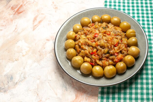 Top view of roasted eggplant salad and pickled plums on plate on nude surface