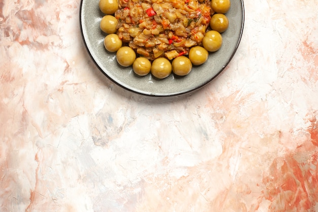 Top view of roasted eggplant salad and pickled plums on plate on nude surface