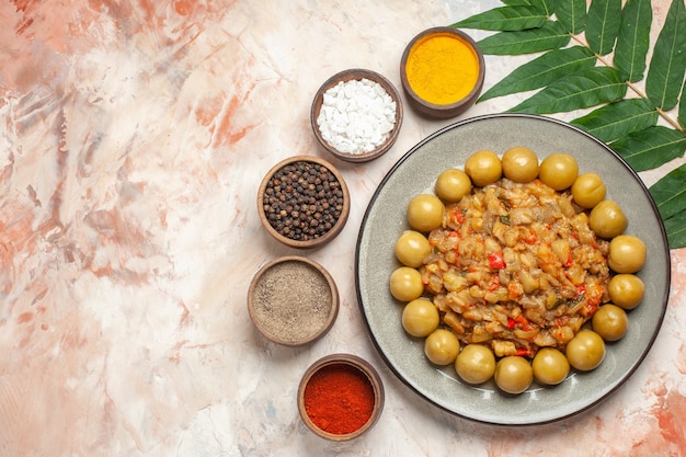 Top view of roasted eggplant salad on plate different spices in small bowls leaves on nude surface