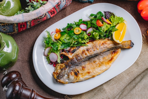 Top view of roasted fish served with fresh vegetables and lemon on a plate
