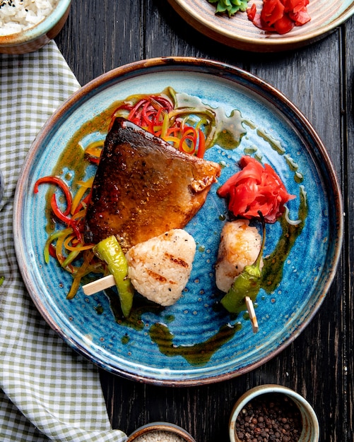 Top view of roasted fish with vegetables pickled ginger slices and soy sauce on a plate on rustic