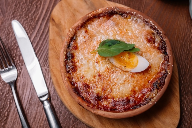 Top view of roasted italian dish in pottery pan garnished with melted cheese and boiled egg halve