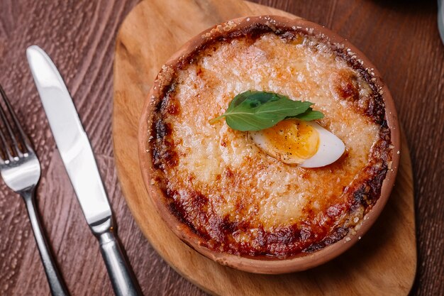 Вид сверху жареного итальянского блюда в кастрюле, украшенный плавленым сыром и половиной вареного яйца