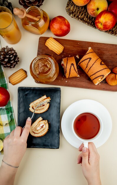 黒のトレイの上に敷設し、紅茶のカップと桃のジャムクッキーの新鮮な熟したネクタリンと白のジュースのガラスとガラスの瓶を保持しているロールケーキのトップビュー