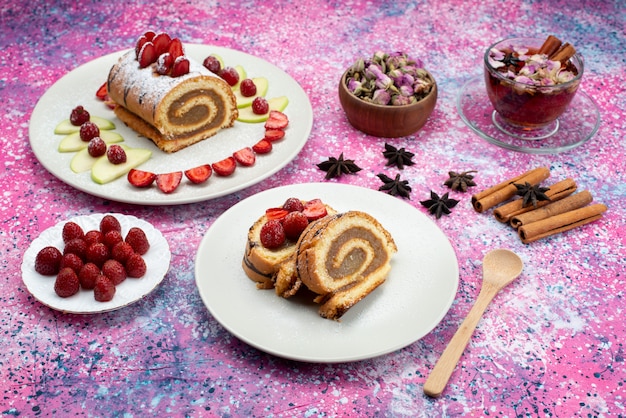Вид сверху ролл кусочки торта с разными фруктами внутри тарелки с чаем на цветном фоне торт бисквит сладкого цвета