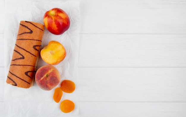 Top view of roll cake with fresh peaches and dried apricots on white with copy space