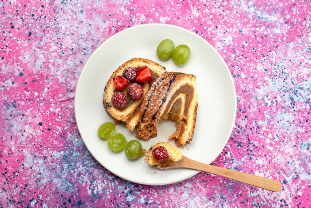 Foto gratuita torta del rotolo di vista superiore con la frutta all'interno del piatto bianco sul colore dolce del biscotto della torta del pavimento viola