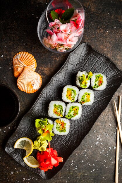 Top view roll set with pickled ginger and wasabi and soy sauce and chopsticks in dark plate