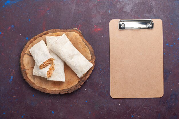 Top view rolled dough with meat filling and notepad on the dark background