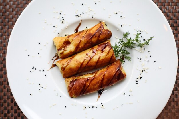 Top view rolled pancakes with sauce and a sprig of dill on a plate