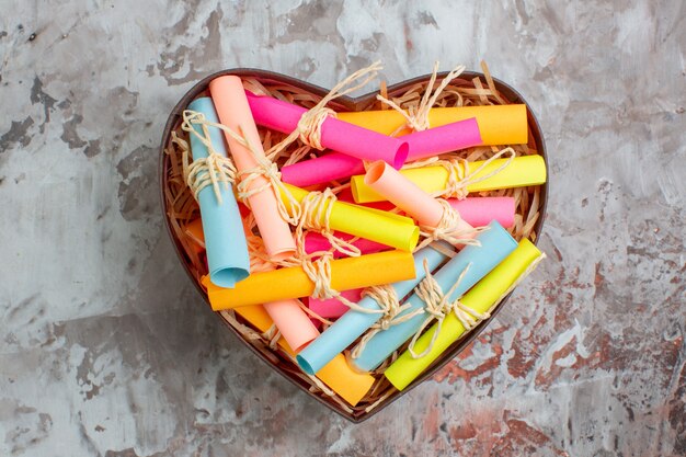 Top view rolled up colored sticky notes tied with rope in heart shaped box on table