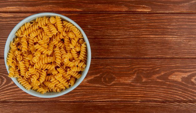 Top view of rotini pasta in bowl on wooden surface with copy space