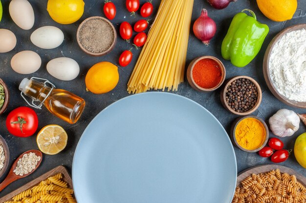 Top view round blue plate with raw pasta flour vegetables seasonings and eggs on dark background food egg dough dinner fruit color
