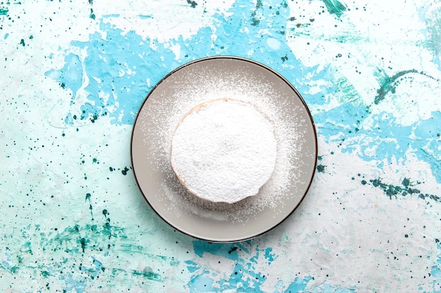 Top view round cake with sugar powder inside plate on light blue surface