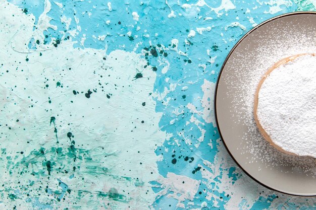 밝은 파란색 표면에 있는 접시 안에 설탕 가루가 있는 위쪽 보기 둥근 케이크