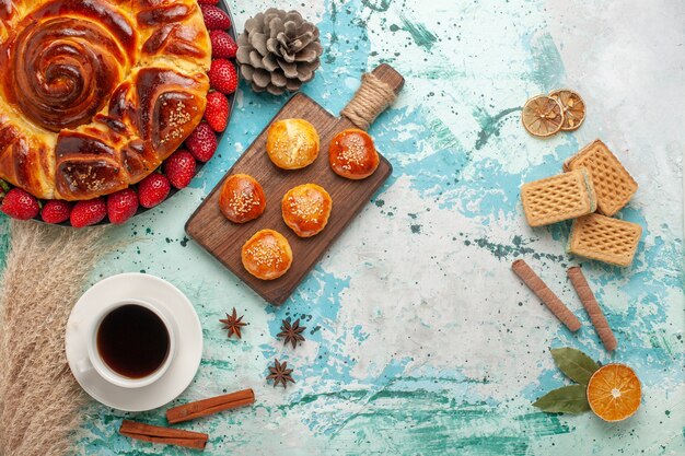 Top view round delicious pie with strawberries waffles and cup of tea on light blue surface