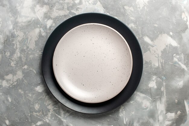 Вид сверху круглой пустой тарелки черного цвета с белой тарелкой на серой поверхности