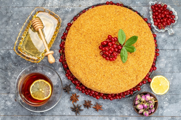 Foto gratuita una torta di miele rotonda di vista superiore deliziosa e al forno con i mirtilli rossi sullo zucchero del biscotto della torta grigia della scrivania infornano