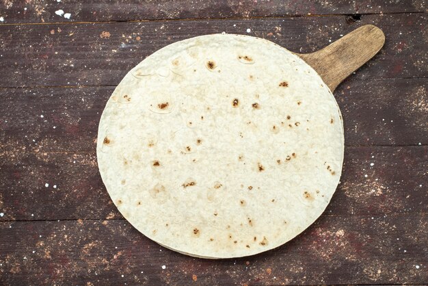 Top view round lavash dough bread like on the brown wooden desk food meal pastry dough