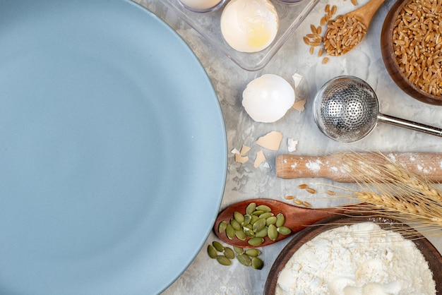 テーブルの上のビオラの木のスプーンの小麦粉と小麦の穀物ボウルの上面図丸皿卵 Premium写真