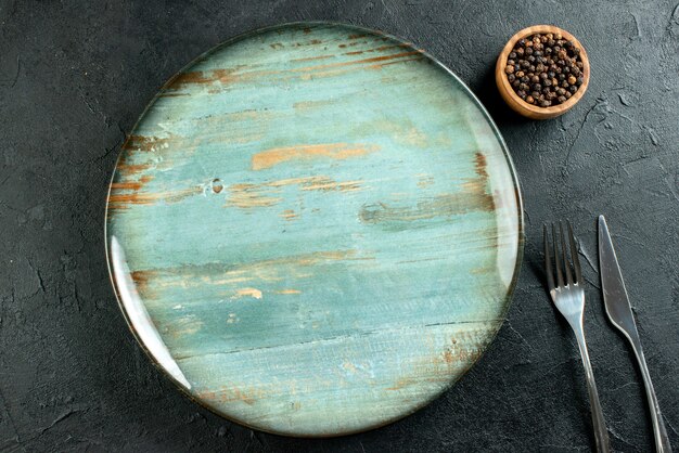 Бесплатное фото Вид сверху круглое блюдо обеденный нож и вилка черный перец в миске на черном столе