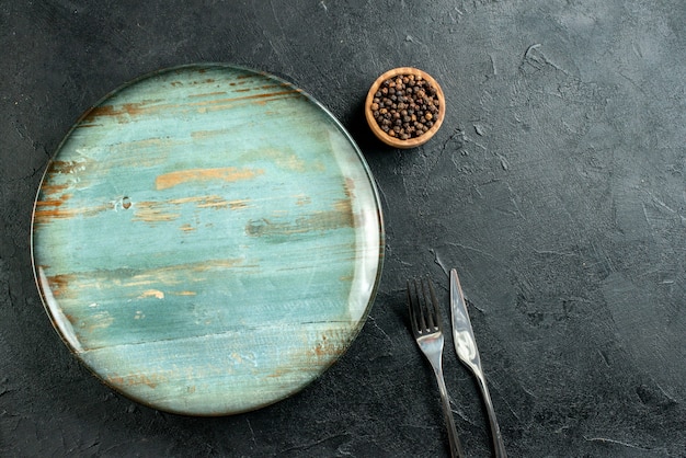 Foto gratuita vista dall'alto piatto rotondo cena coltello e forchetta pepe nero in ciotola sulla tavola nera spazio libero