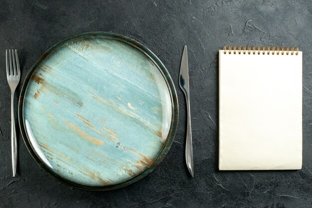 Top view round platter dinner knife and fork notebook on black table